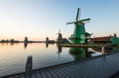 Traditional windmills by canal at zaanse schans against clear sky