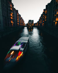 Illuminated buildings by canal against sky in city