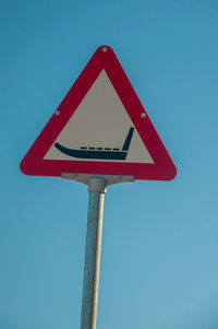 Low angle view of road sign against clear blue sky