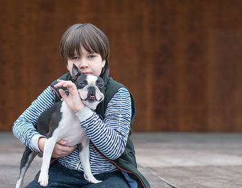 Portrait of boy holding dog sitting outdoors