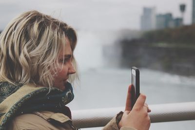 Close-up of woman using mobile phone while standing by railing in city