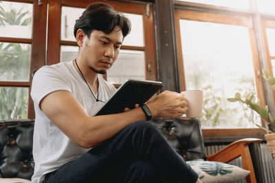 Young man looking through window at home