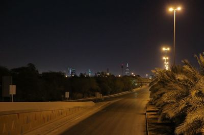 Road by illuminated city against sky at night