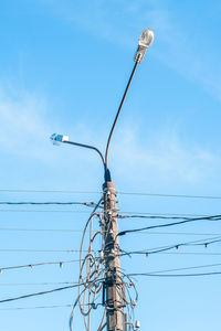 Low angle view of street light and electricity pylon against sky