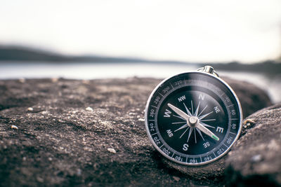 Close-up of navigational compass on stone wall by lake