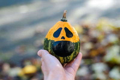 Woman's hand holds a scary halloween pumpkin against the background of autumn foliage.