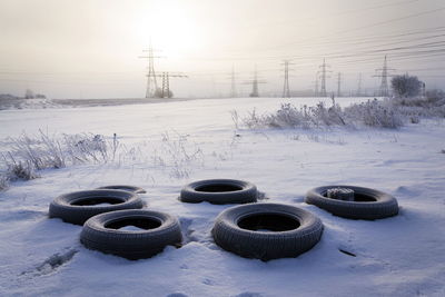 Snow covered field by electricity pylon against sky