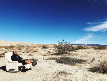Men sitting in desert against blue sky