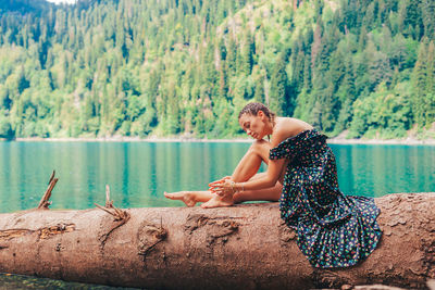 Young woman sitting on rock by lake