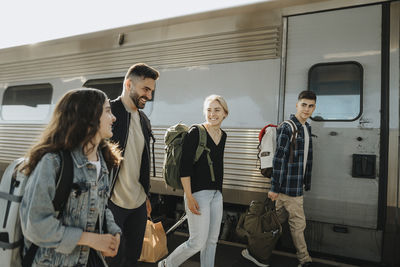 Happy family with luggage walking near train at railroad station