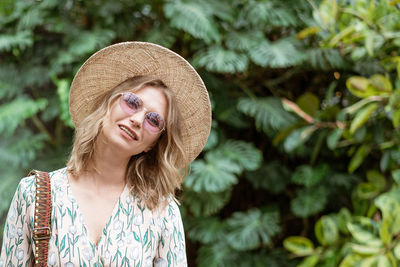 Beautiful young woman in a straw hat and glasses in the park on a background of greenery