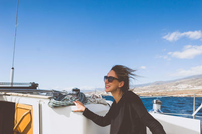 Happy woman with sunglasses on boat in sea against sky
