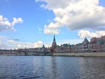 View of buildings by river against cloudy sky