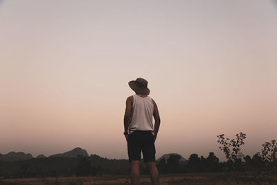 Rear view of man standing on field against sky during sunset