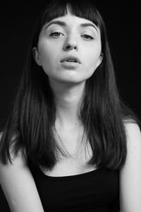 Close-up portrait of young woman looking away while sitting against black background