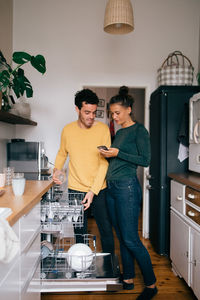 Woman showing mobile phone to boyfriend while standing in kitchen