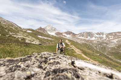 Full length of woman knelling on rock against mountains and sky