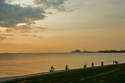 People on sea shore against sky during sunset