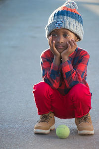 Full length of cute boy crouching in hat with ball looking away