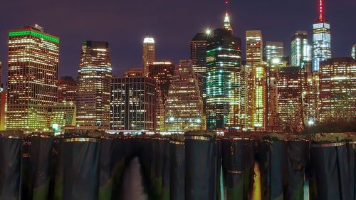 Illuminated modern buildings by river against sky at night