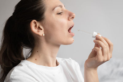 Close-up of young woman holding syringe against white background