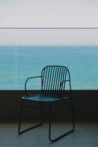 Empty chairs and table against sea against clear sky