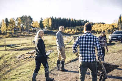 Multi-ethnic male and female farmers with equipment walking on field