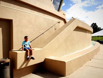 Full length of boy sitting on railing by building