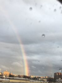 Rainbow over city against cloudy sky