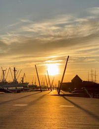 Silhouette cranes at harbor against sky during sunset