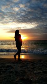 Rear view of woman standing at beach during sunset