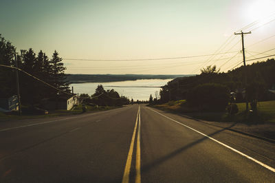 Road by trees against sky during sunset