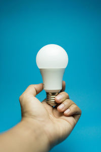 Close-up of hand holding light bulb against blue background