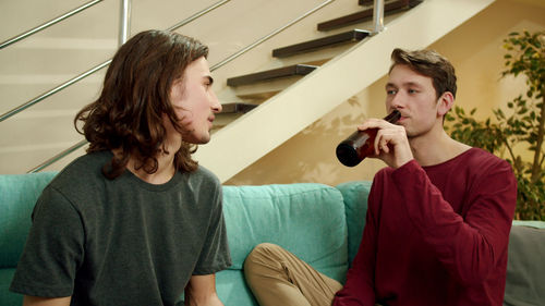 Gay couple drinking while sitting on sofa at home
