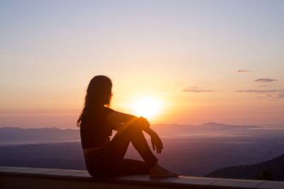 Silhouette man sitting on mountain against sky during sunset