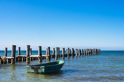 Wooden posts in sea against clear blue sky