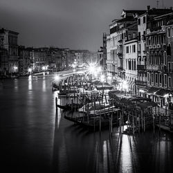 Boats moored at harbor against buildings in city at night