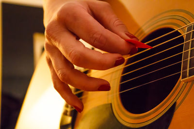 Cropped hand of woman playing guitar at home