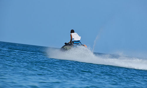 Rear view of man on jet boat over sea against clear sky
