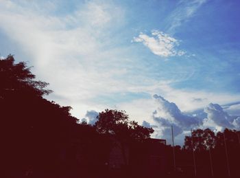 Low angle view of trees against cloudy sky