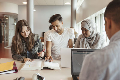 Multi-ethnic friends reading textbook at desk in university