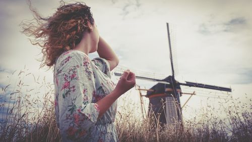 Side view of woman standing on field against sky and windmill