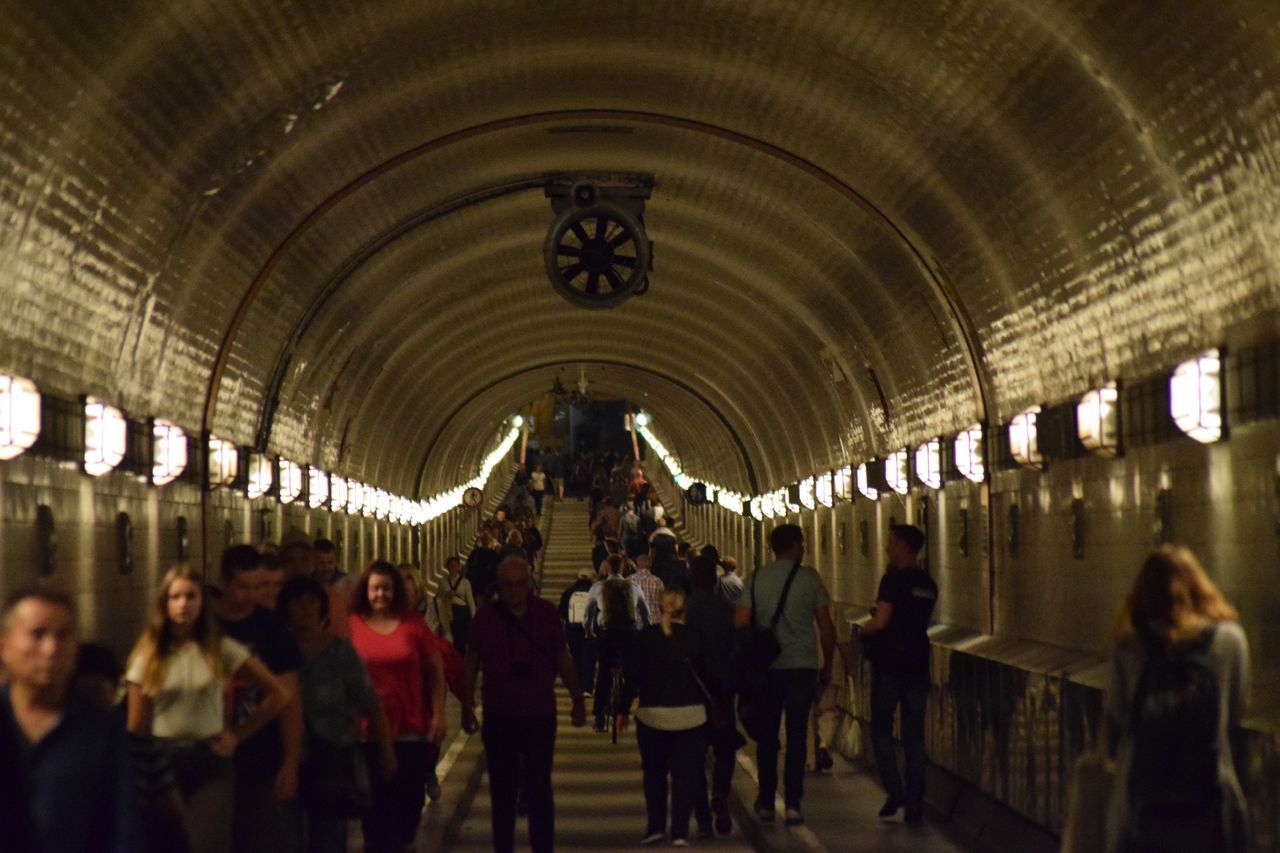 GROUP OF PEOPLE WALKING IN ILLUMINATED UNDERGROUND CORRIDOR