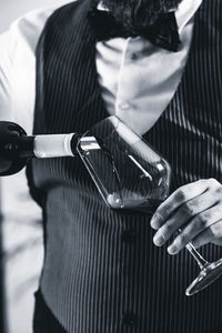 Midsection of bartendar pouring wine in glass