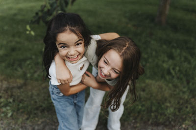 Portrait of playful sisters standing with arm around at park