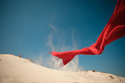 Red scarf waving over sand against blue sky