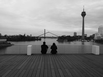 Rear view of couple sitting on promenade by river in city