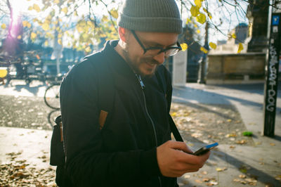 Happy mid adult man using phone on footpath