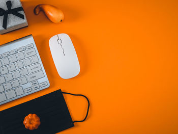 Keyboard, mouse, pumpkins and mask on orange.