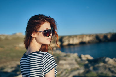 Portrait of young woman wearing sunglasses standing against sky